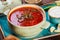 Ukrainian and Russian traditional beetroot soup - borscht in bowl with sour cream, garlic, herbs and bread on wooden background