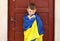 Ukrainian small child stands outdoors supporting homeland, little kid covered in national flag looking at camera