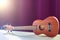 Ukulele is on a white table. Small guitar on purple background. Wooden ukulele in the sunlight