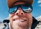 Ultra-wide lens angle portrait shot of high altitude mountain smiling unshaven happy hiker in baseball cap with snow peaks and