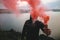 Ultras hooligan holding red smoke bomb in hand, standing on top of rock mountain with amazing view on river. Atmospheric moment.