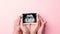 Ultrasound image pregnant baby photo. Woman hands holding ultrasound pregnancy picture on pink background. Pregnancy