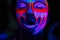 Ultraviolet black light glowing bodyart processing on young woman`s face. Pink and purple dyes in cold blue light