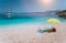 Umbrella and beach accessories on pebble beach on lazy summer day under bright sun light. Sailing boat stays at anchor