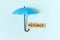 An umbrella and the inscription `home` in wooden letters on a blue background. A symbol of comfort and protection