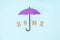 An umbrella and the inscription `home` in wooden letters on a blue background. A symbol of comfort and protection