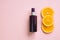 Unbranded brown cosmetic spray bottle and orange slices on pink background. Natural organic spa cosmetics. Body mist oil. Cream