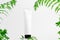 Unbranded container on pedestal. Flacon for lotion, toiletry. Forest fern leaves on light background. Tube for cosmetics. Mockup