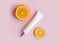Unbranded face and eye cream squeeze cosmetic tube with long nozzle and bronze screw cap and orange slices on pink background.