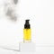 Unbranded glass container with dispenser on shadow background. Transparent bottle with oil for body on stand. Face serum