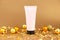 Unbranded pink face cream squeeze cosmetic tube with black cap, gold christmas balls and paper firecracker pieces on golden