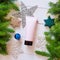 Unbranded pink squeeze bottle cosmetic tube with black cap and Christmas stars, toys and spruce branches on wooden white table.