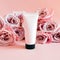 Unbranded pink squeeze bottle cosmetic tube with black screw cap and pink roses on pink background. Bottle for branding and label