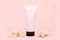 Unbranded pink squeeze bottle cream tube with black screw cap and a lot of different sea shells on pink background. Mockup with