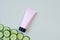 Unbranded pink squeeze cosmetic tube with black screw cap and cucumber slices on light green background. Skincare and advertising