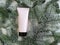 Unbranded pink squeeze cosmetic tube with black screw cap on snowy branches of christmas fir tree. Mockup, template. Skin care,