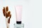 Unbranded pink squeeze cream tube with black screw cap on glass stand and bunch of brown herbs Lagurus. Cosmetic bottle for