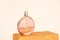 Unbranded round glass perfume bottle on golden podium on ivory background. Eau de toilette. Mockup, copy space