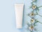 Unbranded white squeeze bottle cosmetic cream tube and line frame border of blue Nigella flowers on pastel blue background.