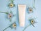 Unbranded white squeeze bottle cosmetic cream tube and round frame border of blue Nigella flowers on pastel blue background.
