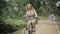 Uncertain senior Caucasian woman riding bike in summer park. Cheerful funny middle aged lady losing control and stopping