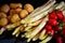 Uncooked asparagus, potatos and strawberries in front of a black background like a stil