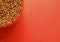 Uncooked buckwheat in a container on a red background in the corner