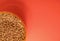 Uncooked buckwheat in a container on a red background in the corner