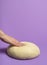 Uncooked dough isolated on purple table. Woman hand pressing the dough