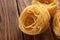 Uncooked fettuccine pasta ball, on textured wooden background.