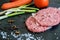 Uncooked fresh hamburgers with carrot, tomatoes, green garlic and spices on the black kitchen board prapared for cookin closeup