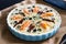 Uncooked millet quiche with salmon, spinach and black olives in cooking pan on wooden table