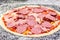 Uncooked pizza with sliced salami, ham and sausages.