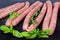 Uncooked pork sausages and fresh herbs on black surface closeup