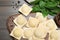 Uncooked ravioli, basil and peppercorns on wooden table, closeup