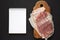 Uncooked Raw Bacon on a rustic wooden board, blank notepad on a black surface, top view. Flat lay, from above, overhead