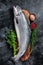 Uncooked raw sea salmon whole fish on a wooden board with herbs. Black background. Top view