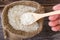 Uncooked rice in a wooden spoon over small burlap sack.