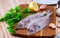 Uncooked roosterfish with greens and garlic on wooden board