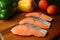 Uncooked sliced salmon on a wooden cutting board with colorful vegetables in Background