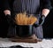 Uncooked yellow long spaghetti in a black metal pan and a chef in a striped apron