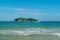 Under the blue sky and white clouds, the waves wash on the beach, and the small island in the distance