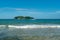 Under the blue sky and white clouds, the waves wash on the beach, and the small island in the distance