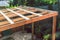 Under construction garden pergola with wooden structure in sunny backyard surrounded by tropical plants