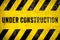 Under construction warning sign text with yellow black stripes painted over concrete wall cement facade texture background