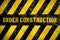 Under construction warning sign with yellow and dark stripes painted over concrete wall coarse facade as texture background
