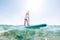 Under the water view angle to the smiling blonde teenager boy rowing stand up paddle board. Active family summer vacation time