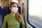 Undergraduate student on public transport wearing mandatory medical face mask looking through the window