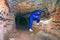 Underground work. Hunched worker in a blue overall and a safety helmet stands in tunnel.