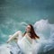 Underwater girl. Beautiful red-haired woman in a white dress, swimming under water.